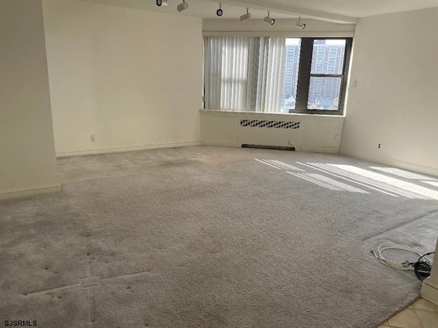 carpeted spare room featuring radiator heating unit and track lighting