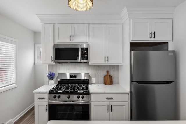 kitchen with light stone countertops, appliances with stainless steel finishes, white cabinets, and backsplash