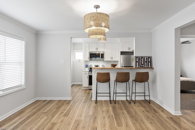 kitchen with a breakfast bar area, hanging light fixtures, appliances with stainless steel finishes, light hardwood / wood-style floors, and white cabinets