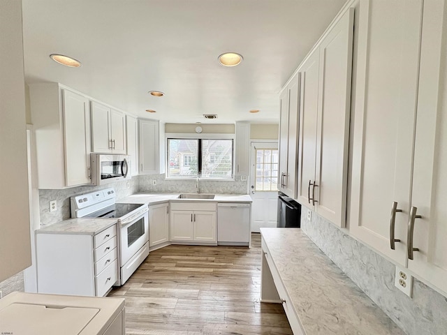 kitchen featuring white cabinetry, sink, light wood-type flooring, backsplash, and white appliances