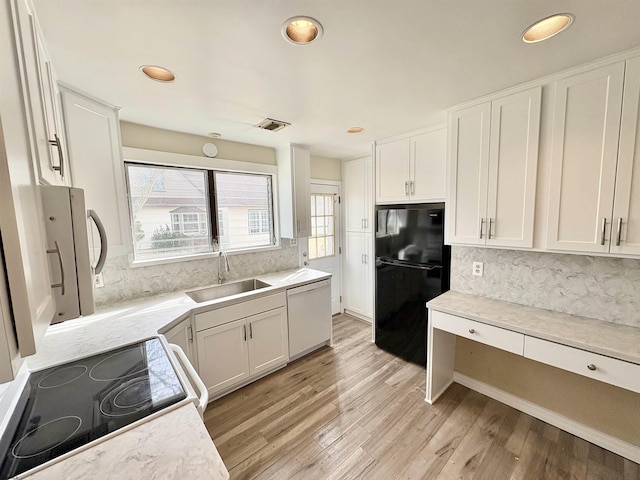 kitchen with sink, black fridge, white dishwasher, white cabinets, and stove