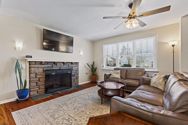 living room with dark hardwood / wood-style floors, ceiling fan, and a stone fireplace