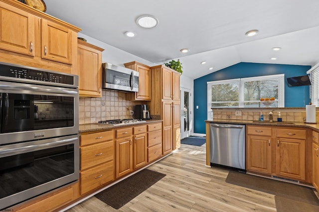 kitchen featuring sink, light hardwood / wood-style flooring, appliances with stainless steel finishes, vaulted ceiling, and dark stone counters