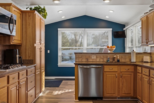 kitchen featuring lofted ceiling, sink, hardwood / wood-style floors, stainless steel appliances, and decorative backsplash