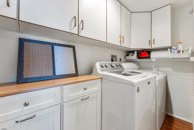 clothes washing area featuring hardwood / wood-style flooring, washing machine and dryer, and cabinets