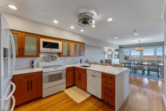 kitchen with sink, decorative light fixtures, kitchen peninsula, white appliances, and light hardwood / wood-style floors