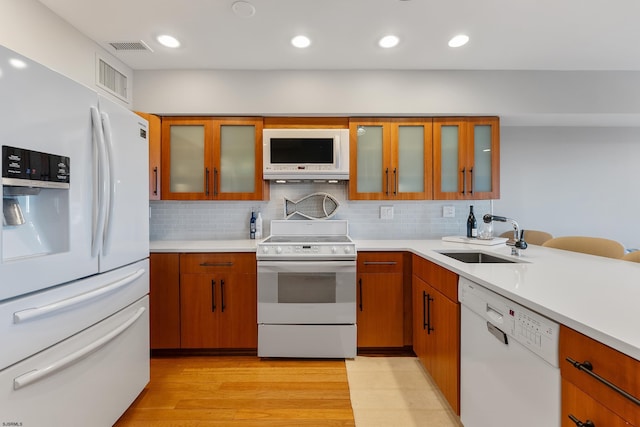 kitchen featuring sink, backsplash, white appliances, and light wood-type flooring