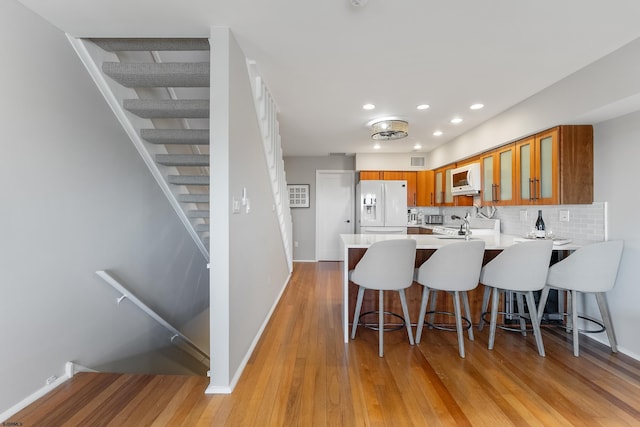 kitchen featuring white appliances, a kitchen breakfast bar, tasteful backsplash, kitchen peninsula, and light wood-type flooring