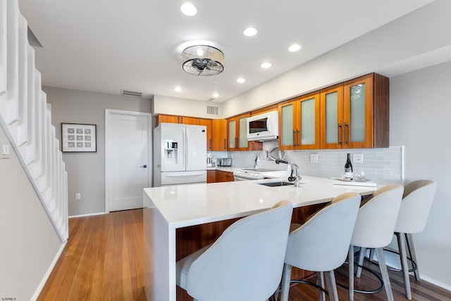 kitchen featuring sink, backsplash, a kitchen bar, kitchen peninsula, and white appliances