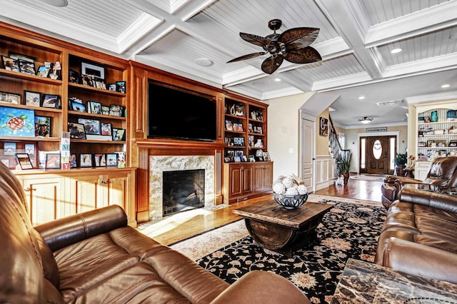 living room featuring a premium fireplace, hardwood / wood-style floors, coffered ceiling, ornamental molding, and built in shelves