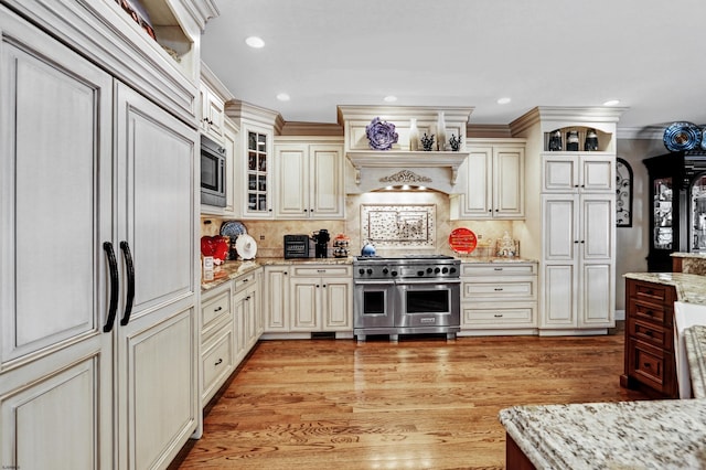 kitchen with built in appliances, light stone countertops, light hardwood / wood-style floors, and cream cabinetry