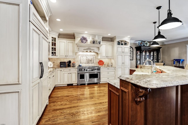 kitchen featuring light stone counters, decorative light fixtures, a large island with sink, ornamental molding, and double oven range