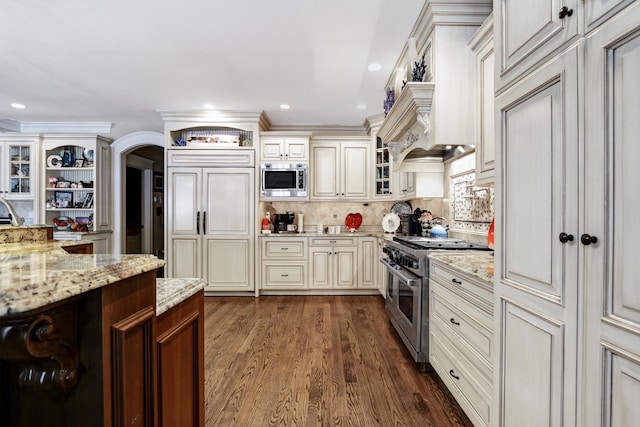 kitchen with dark hardwood / wood-style flooring, decorative backsplash, light stone countertops, built in appliances, and cream cabinets