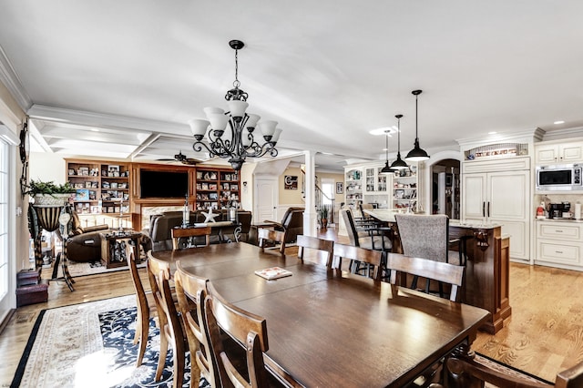 dining area featuring built in shelves, ornate columns, crown molding, light hardwood / wood-style floors, and ceiling fan with notable chandelier