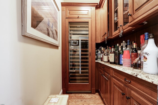 bar featuring wine cooler, light stone countertops, and light hardwood / wood-style floors