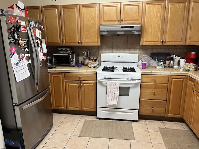 kitchen with light tile patterned floors, tile counters, stainless steel refrigerator, and white gas stove