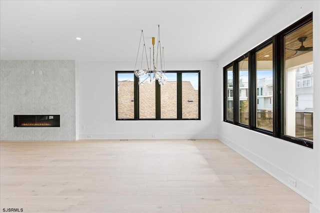 unfurnished dining area with a notable chandelier, a fireplace, and light hardwood / wood-style floors