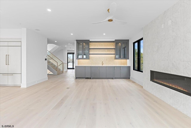 unfurnished living room with a fireplace, ceiling fan, and light wood-type flooring