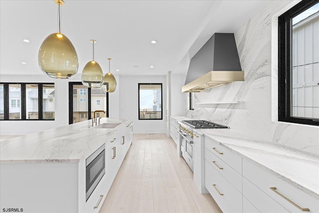 kitchen with premium range hood, stainless steel microwave, decorative light fixtures, sink, and white cabinets