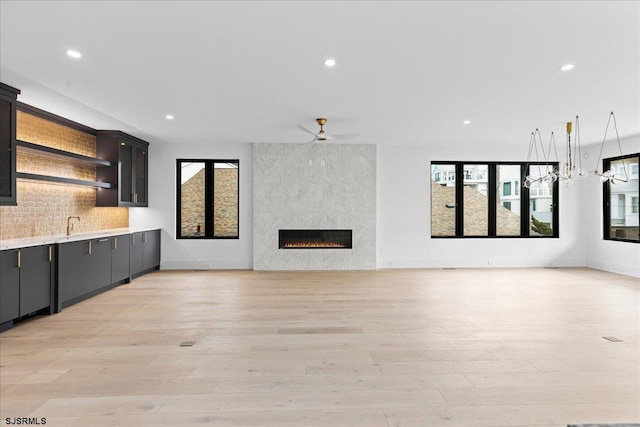 unfurnished living room featuring a wealth of natural light, a fireplace, ceiling fan, and light wood-type flooring