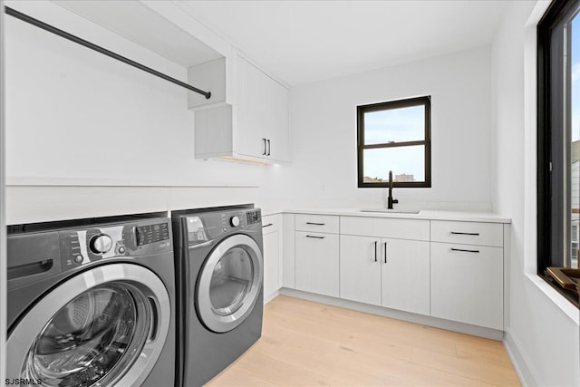 clothes washing area featuring cabinets, separate washer and dryer, sink, and light wood-type flooring