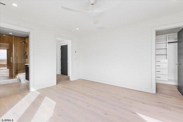 unfurnished bedroom featuring ceiling fan, connected bathroom, a walk in closet, a closet, and light wood-type flooring