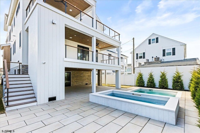 back of house with an in ground hot tub, a balcony, and a patio