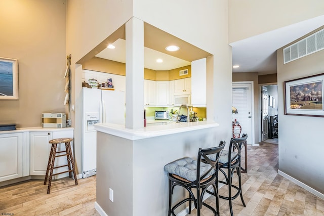 kitchen with a breakfast bar, white cabinetry, a high ceiling, white fridge with ice dispenser, and kitchen peninsula