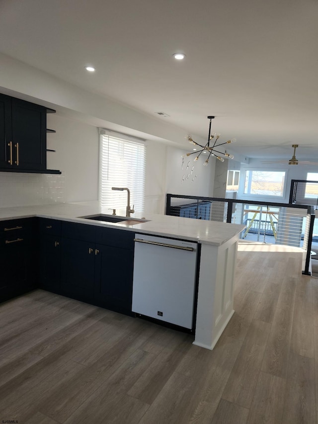 kitchen with white dishwasher, sink, kitchen peninsula, and a healthy amount of sunlight