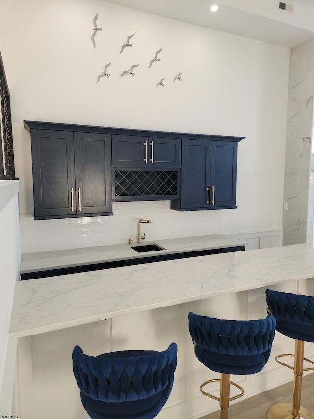 bar with blue cabinets, sink, light stone counters, tasteful backsplash, and wood-type flooring