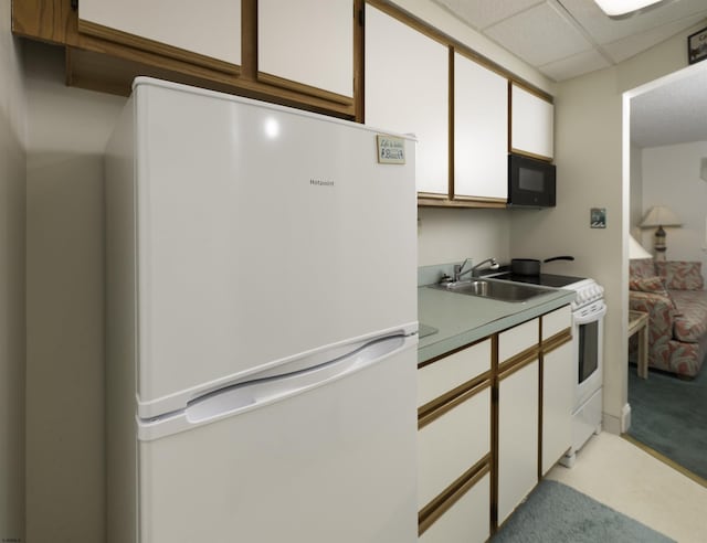 kitchen featuring sink, white cabinetry, a paneled ceiling, light carpet, and white appliances