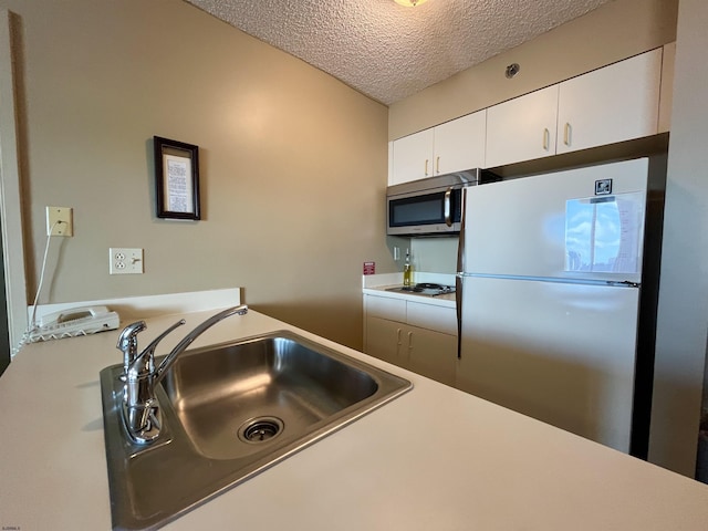 kitchen with sink, refrigerator, white cooktop, a textured ceiling, and white cabinets