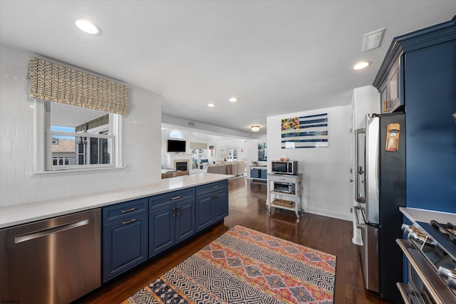 kitchen with blue cabinets, decorative backsplash, dark wood-type flooring, and appliances with stainless steel finishes