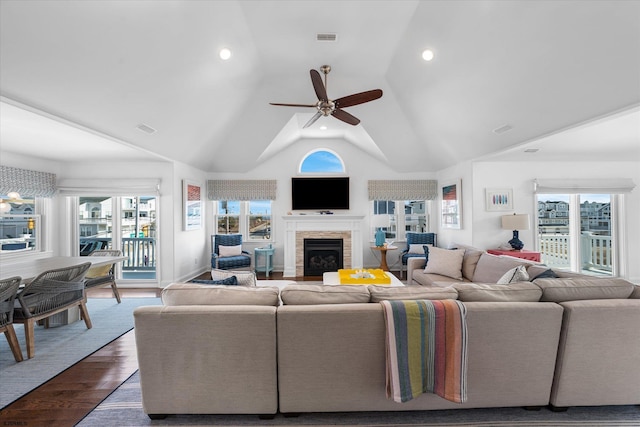 living room with hardwood / wood-style flooring, ceiling fan, a stone fireplace, and high vaulted ceiling