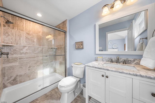 bathroom featuring a shower with door, vanity, and toilet