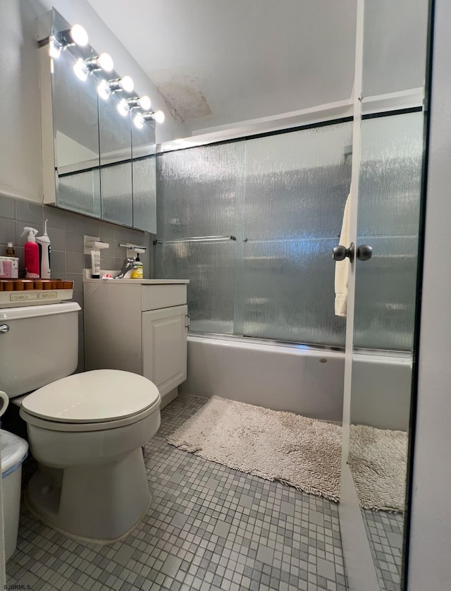 full bathroom with bath / shower combo with glass door, tile walls, tile patterned flooring, vanity, and toilet