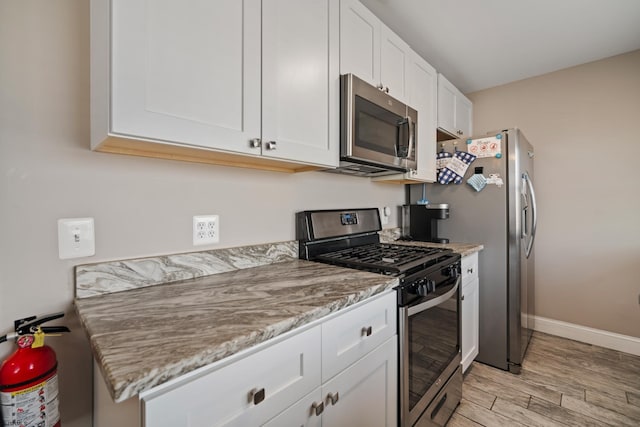 kitchen with stainless steel appliances, white cabinetry, light stone counters, and light hardwood / wood-style flooring