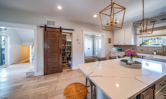 kitchen with a breakfast bar, white cabinets, hanging light fixtures, a center island, and a barn door