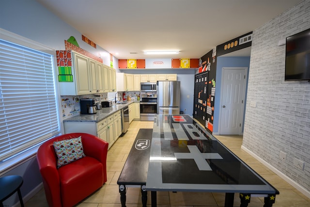 kitchen with light tile patterned floors, sink, stainless steel appliances, light stone countertops, and brick wall