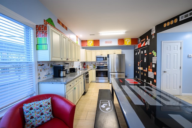 kitchen featuring appliances with stainless steel finishes, sink, light stone counters, and cream cabinetry