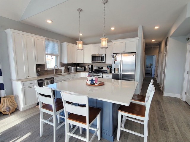 kitchen with stainless steel appliances, a kitchen island, a sink, white cabinetry, and backsplash