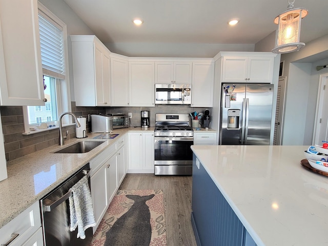 kitchen featuring light wood finished floors, tasteful backsplash, appliances with stainless steel finishes, white cabinets, and a sink