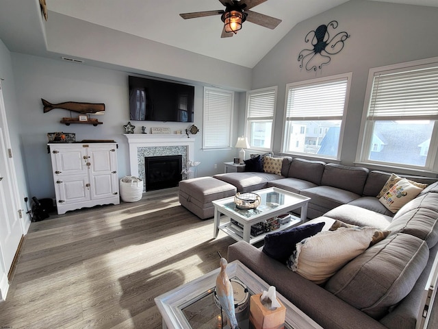 living room with lofted ceiling, visible vents, a tiled fireplace, a ceiling fan, and wood finished floors