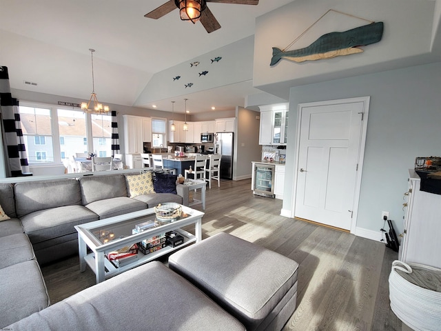 living room with wine cooler, ceiling fan with notable chandelier, wood finished floors, baseboards, and vaulted ceiling