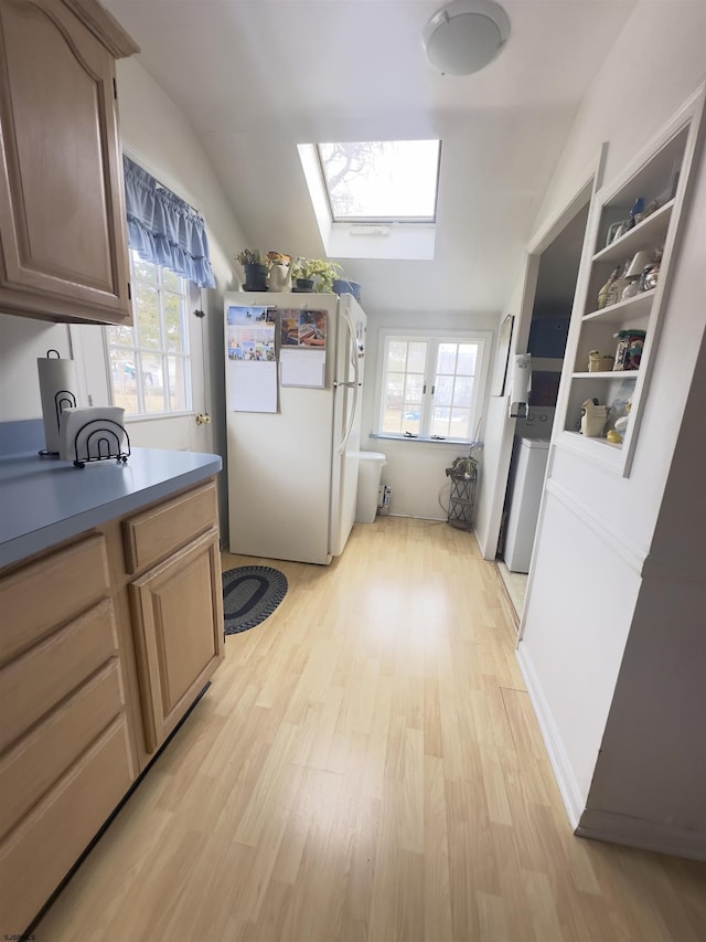 kitchen with white refrigerator, plenty of natural light, lofted ceiling with skylight, and light hardwood / wood-style floors