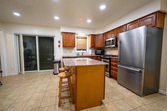 kitchen with light tile patterned flooring, a kitchen island, appliances with stainless steel finishes, tasteful backsplash, and a breakfast bar area