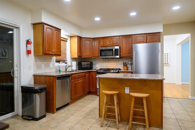 kitchen featuring a kitchen island, appliances with stainless steel finishes, sink, backsplash, and light tile patterned floors