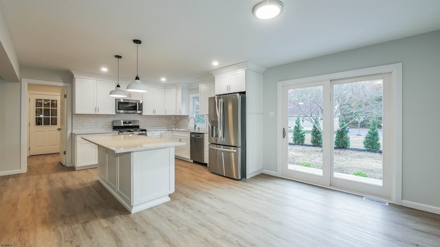 kitchen featuring a kitchen island, decorative light fixtures, tasteful backsplash, white cabinets, and stainless steel appliances