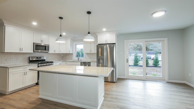 kitchen with light stone counters, decorative light fixtures, a center island, appliances with stainless steel finishes, and white cabinets