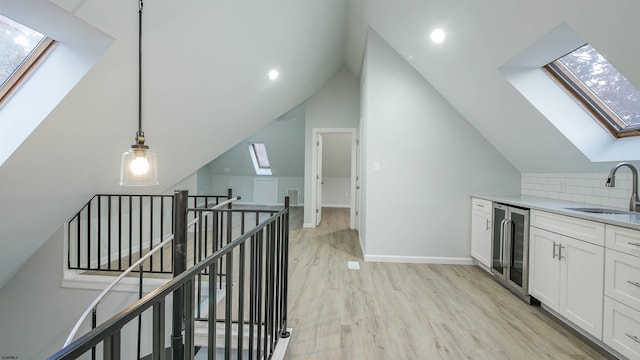 kitchen featuring white cabinetry, sink, wine cooler, hanging light fixtures, and light hardwood / wood-style floors